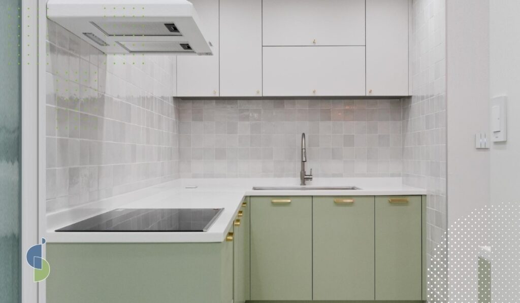 Cocina compacta con gabinetes altos blancos y bajos en verde salvia con herrajes dorados