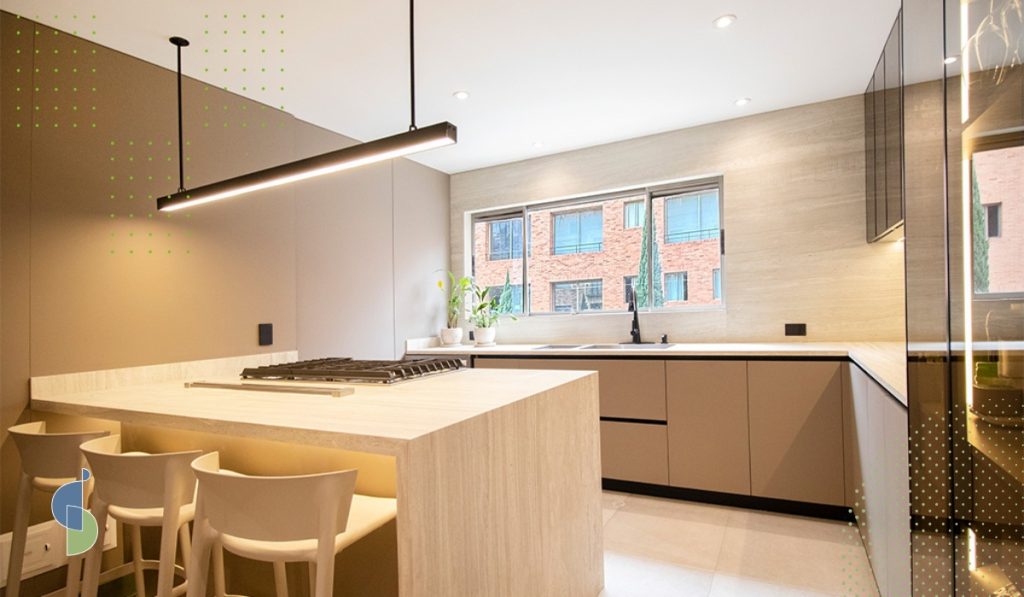 Isla de cocina en tono beige con mesón en piedra clara y lámpara lineal colgante negra