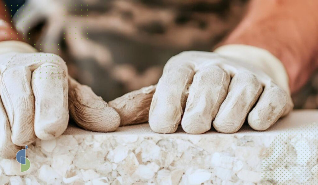 Manos con guantes aplicando sellador en el canto de un mesón de terrazo