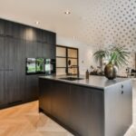 Cocina moderna con mesón de porcelánico ultradelgado gris oscuro, isla central, gabinetes negros de madera y diseño minimalista contemporáneo