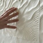 Mano tocando revestimiento cerámico con relieve 3D en ondas blancas
