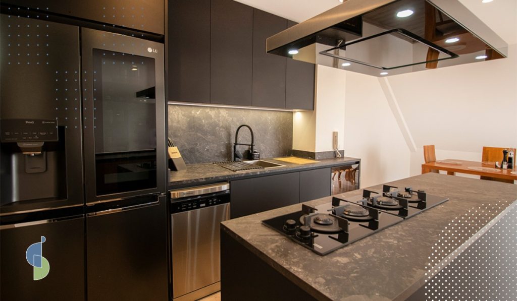 Cocina en tonos oscuros con lavavajillas, nevera de doble puerta y campana de isla junto al comedor