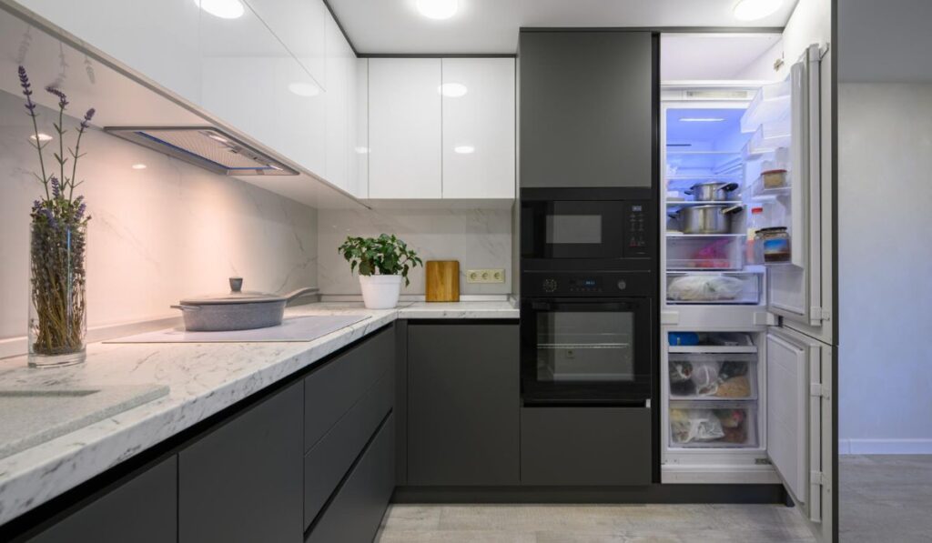 Cocina minimalista en tonos gris y blanco, donde se aprecia una nevera empotrada con un panel frontal a juego con los muebles, logrando una integración elegante y discreta.