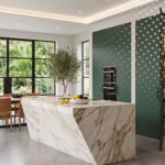 Cocina de lujo con isla de mármol y walk-in pantry con puerta verde camuflada abierta
