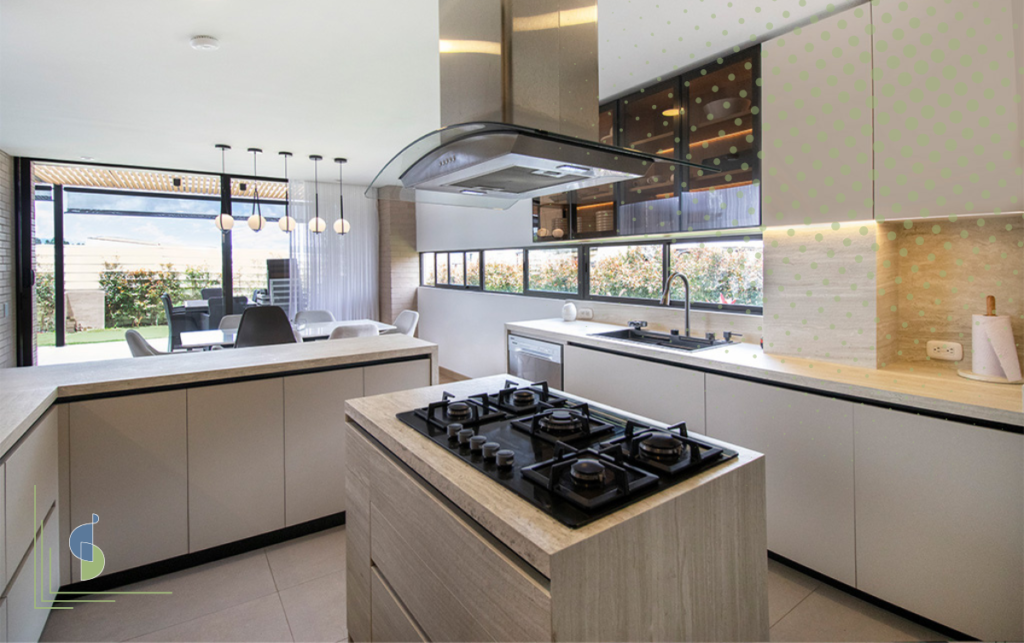Cocina integral abierta con isla central en madera clara y campana de vidrio suspendida