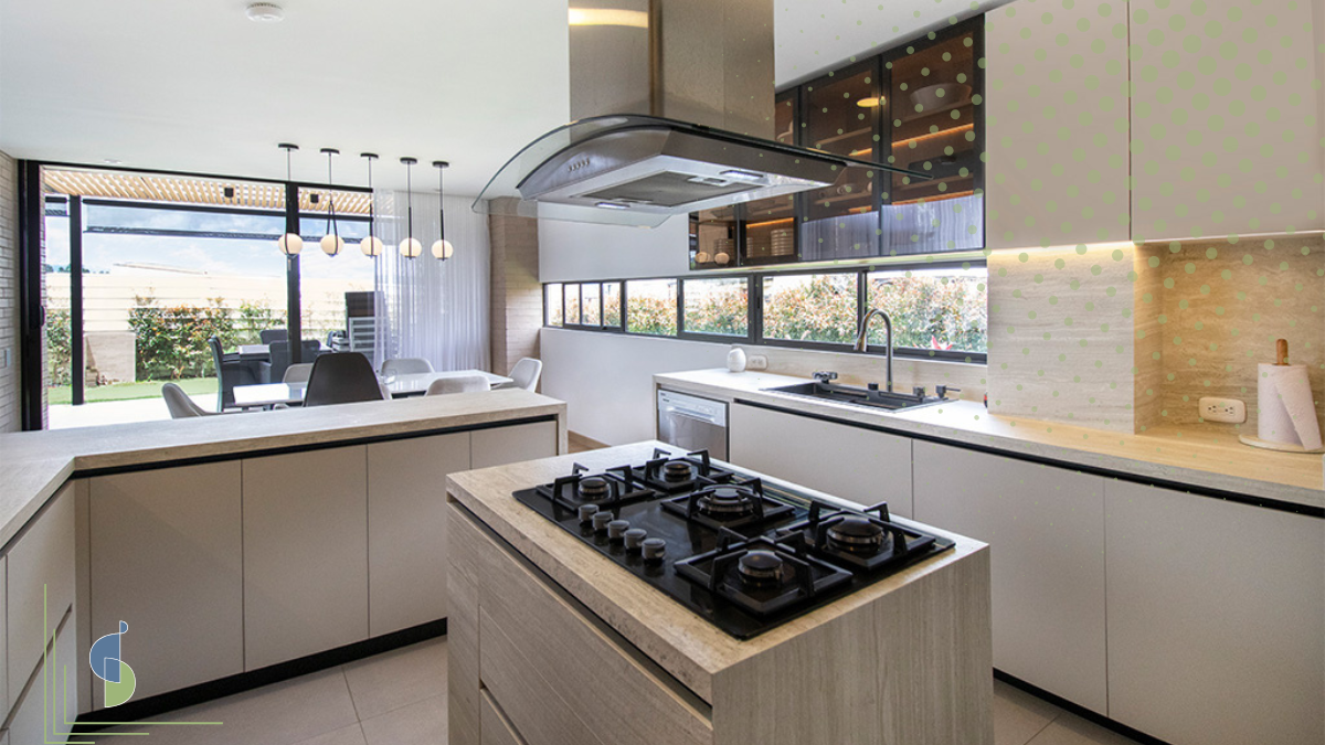 Cocina integral abierta con isla central en madera clara y campana de vidrio suspendida