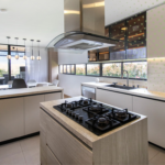 Cocina integral abierta con isla central en madera clara y campana de vidrio suspendida