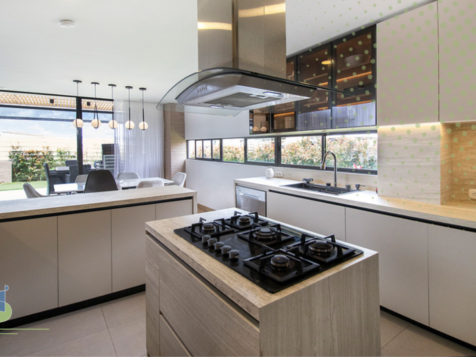 Cocina integral abierta con isla central en madera clara y campana de vidrio suspendida
